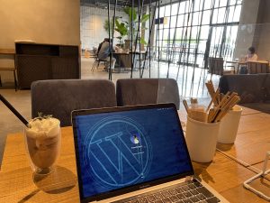A laptop screen showing the WordPress logo, next to a cup of iced coffee in a café